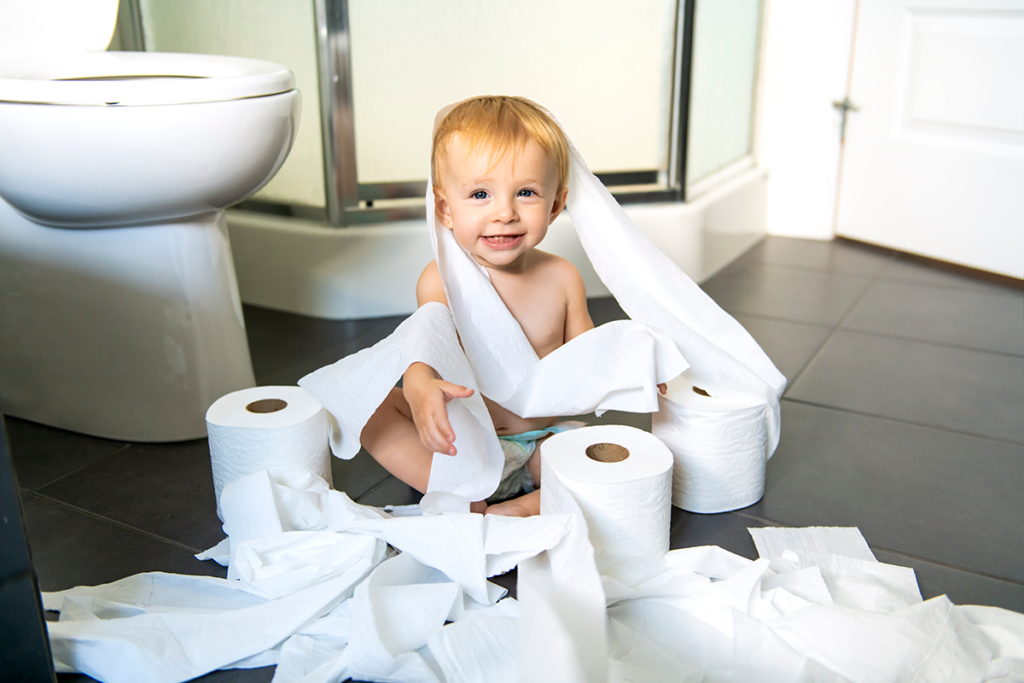 A toddler sitting among several unwound rolls of toilet paper