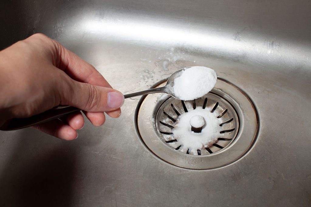 A spoon scooping drain chemicals into a kitchen drain