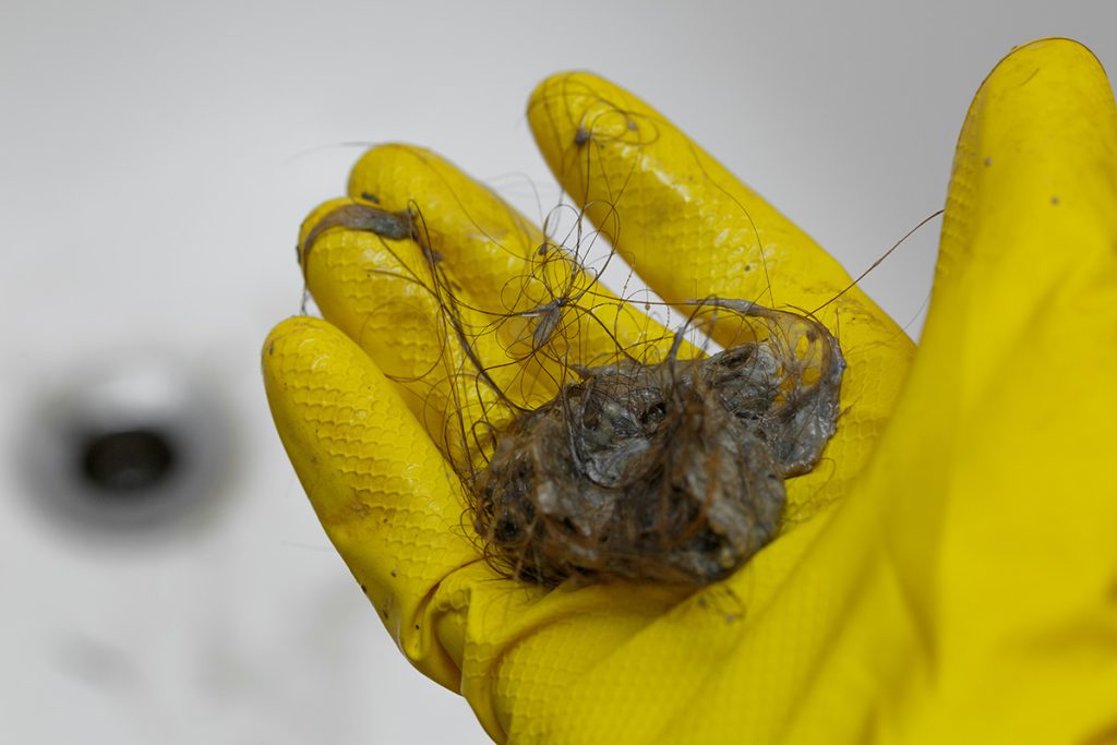 A hand wearing a yellow rubber glove holding hair that clogged a drain