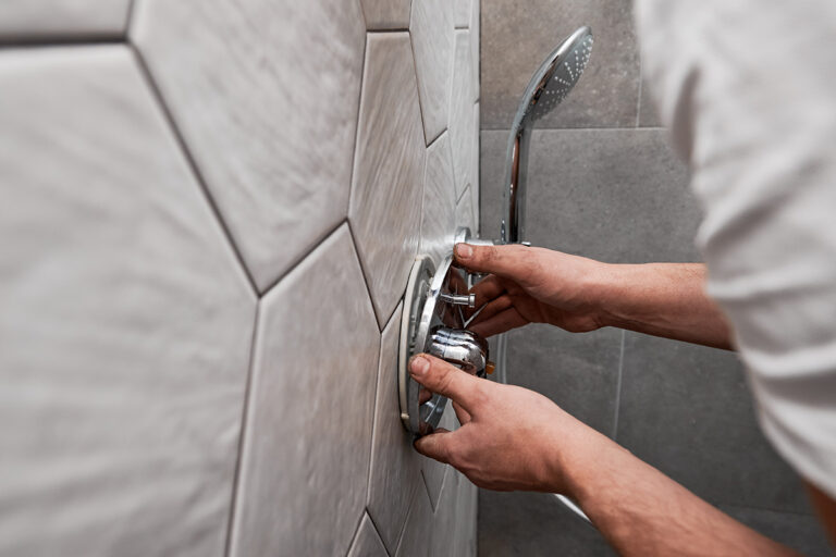 Close up of man standing by the wall with ceramic tile and installing shower faucet with metal handle